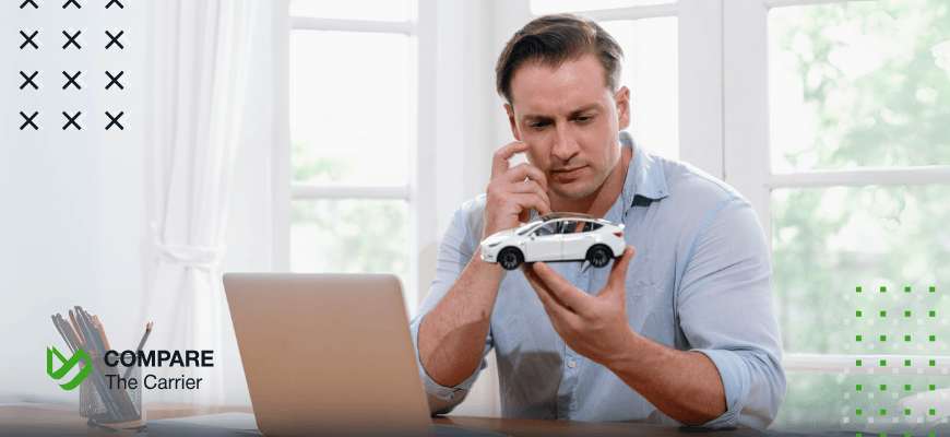 best online car sites A man sits at a desk, holding a small model car while looking thoughtfully at a laptop, symbolizing the consideration and research involved in deciding to buy a car online. The Compare The Carrier logo is in the foreground.