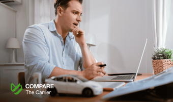 A man looks thoughtfully at a laptop screen, with a white model car on the desk in the foreground, representing the process of researching or buying a car online. The Compare The Carrier logo is visible.