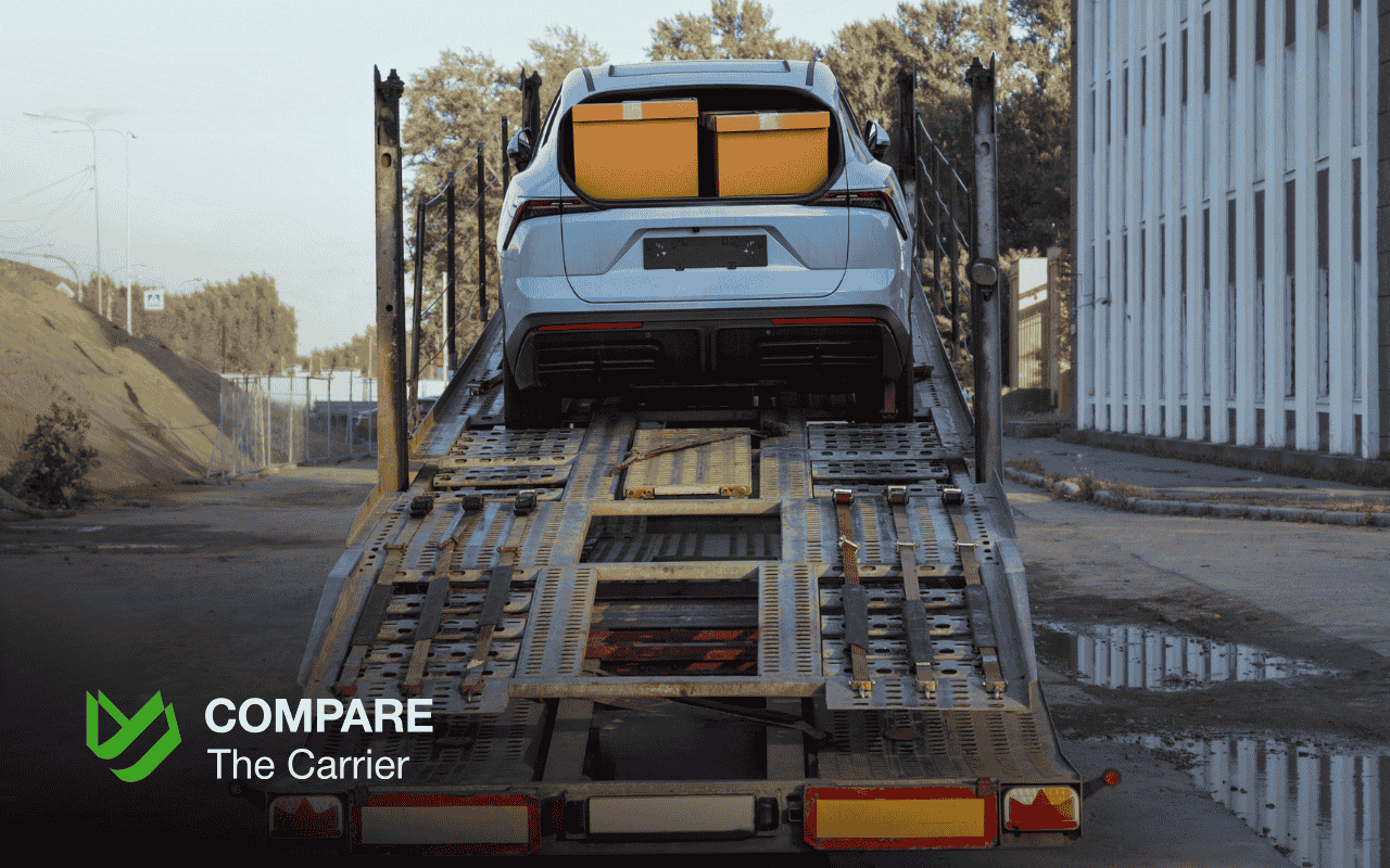Silver SUV with two cardboard boxes on its roof being loaded onto an auto transport carrier, illustrating policies for car shipping with personal items