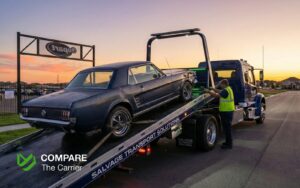Flatbed truck winching a damaged salvage car at an auction site.